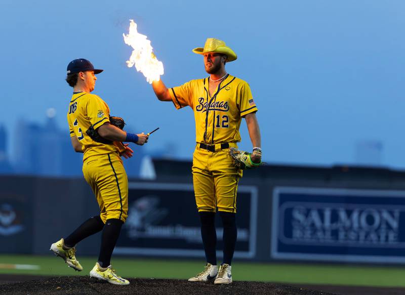 NEW YORK, NEW YORK - AUGUST 11:  Kyle Luigs #12 of the Savannah Bananas has his ball lit on fire by his teammate Eric Jones Jr. #3 before he pitches it during their game against the Staten Island Ferryhawks at Richmond County Bank Ball Park on August 11, 2023 in New York City.  The Savannah Bananas were part of the Coastal Plain League, a summer collegiate league, for seven seasons. In 2022, the Bananas announced that they were leaving the Coastal Plain League to play Banana Ball year-round. Banana Ball was born out of the idea of making baseball more fast-paced, entertaining, and fun.   (Photo by Al Bello/Getty Images)