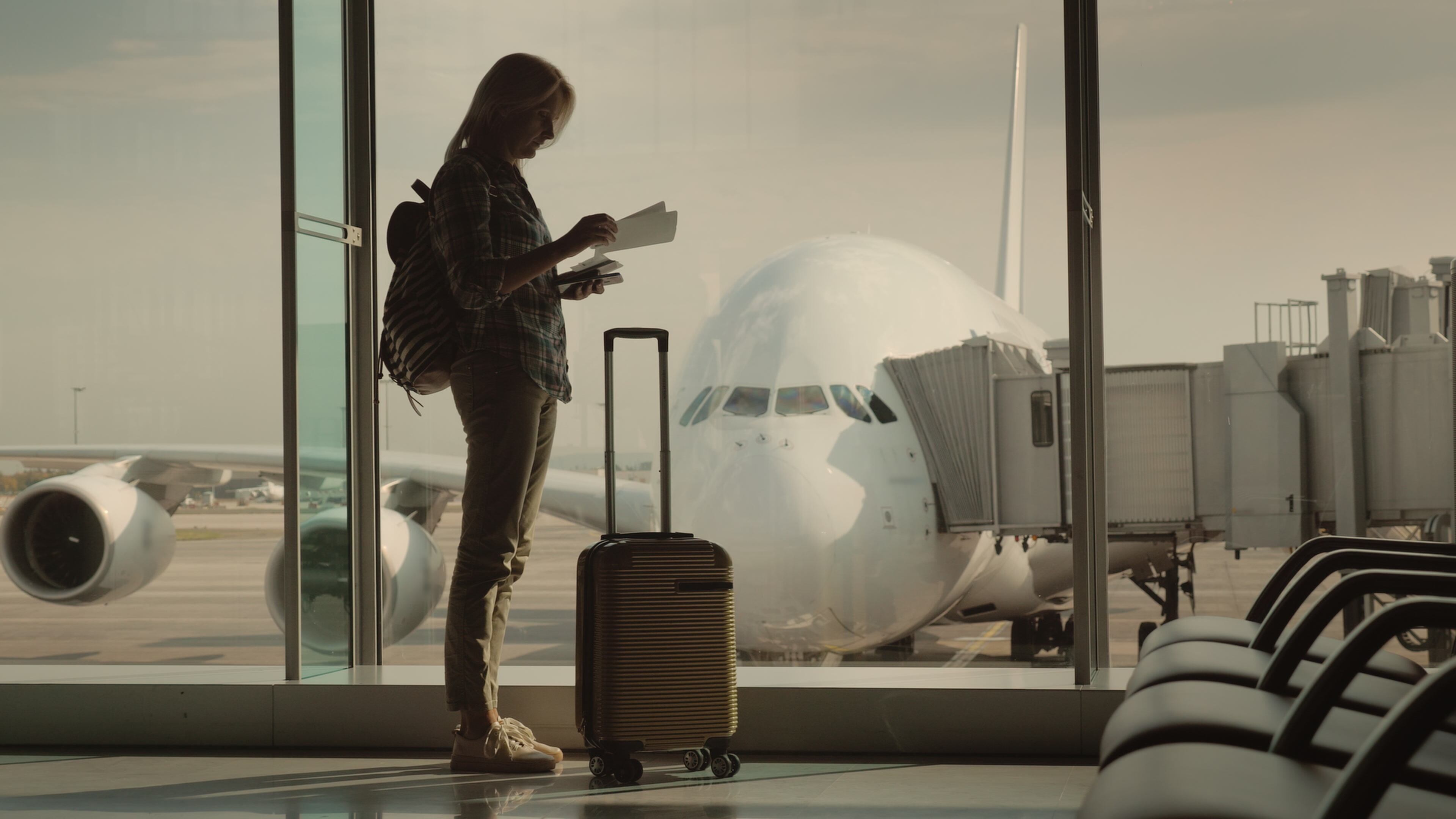A woman with a passport and a boarding pass is standing at the huge window, behind which you can see the airliner. Start of the journey.