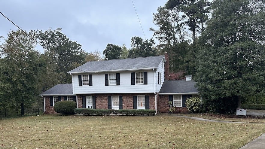 A two-story home is seen, the top half is painted white. The bottom half is brick.
