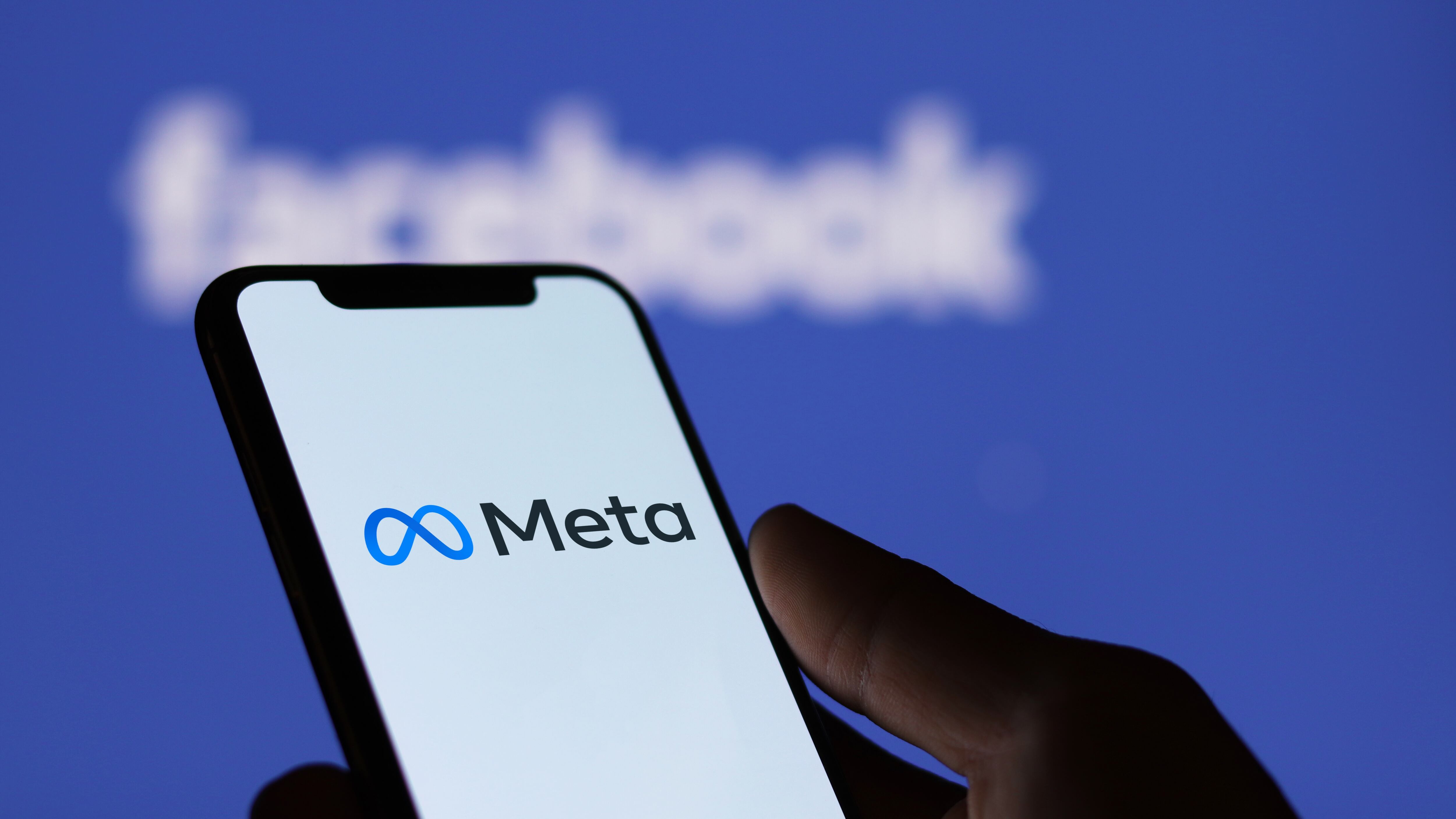Meta logo on smartphone screen and Facebook logo background