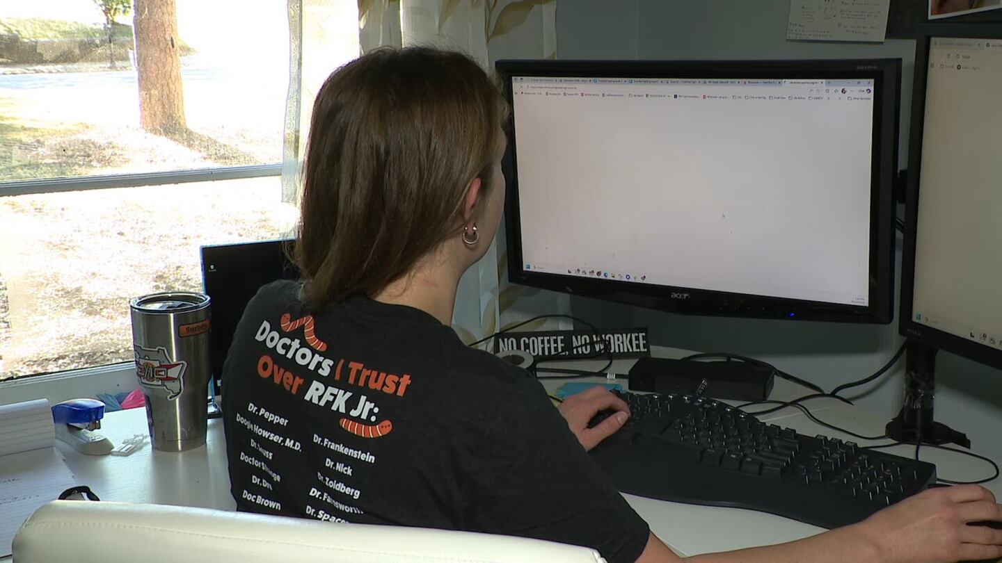 A woman with an anti-RFK shirt sits at a computer.