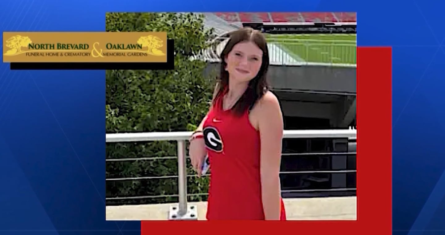 Image shows a young woman wearing a sleeveless red blouse with a Georgia G. She appears to be standing in front of a football stadium.