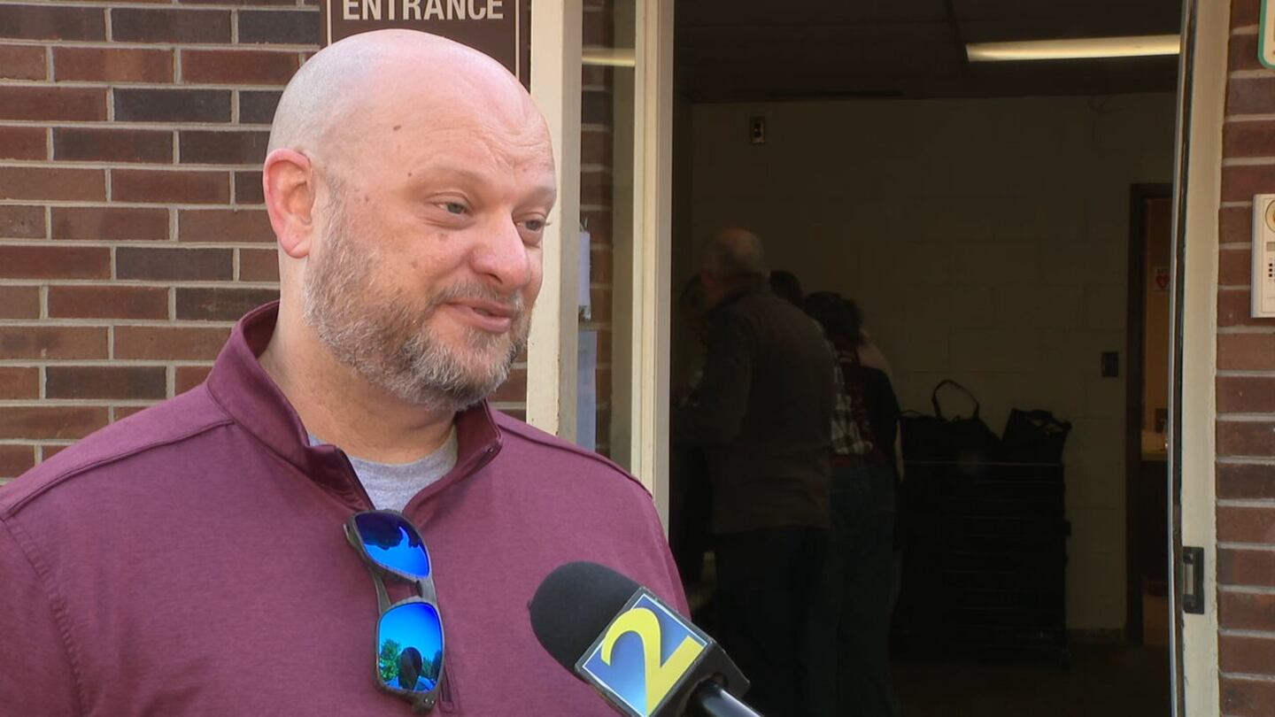 A man is seen in a purple shirt with sunglasses attached to the shirt. He is facing his right.